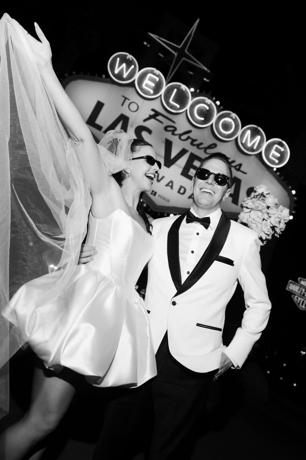 Black and white photo of a bride and groom posing in front of the Welcome to Fabulous Las Vegas sign.