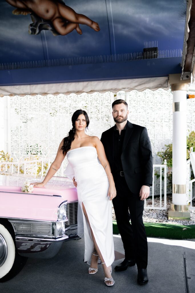 Bride and groom posing with the pink Cadillac at The Little White Chapel