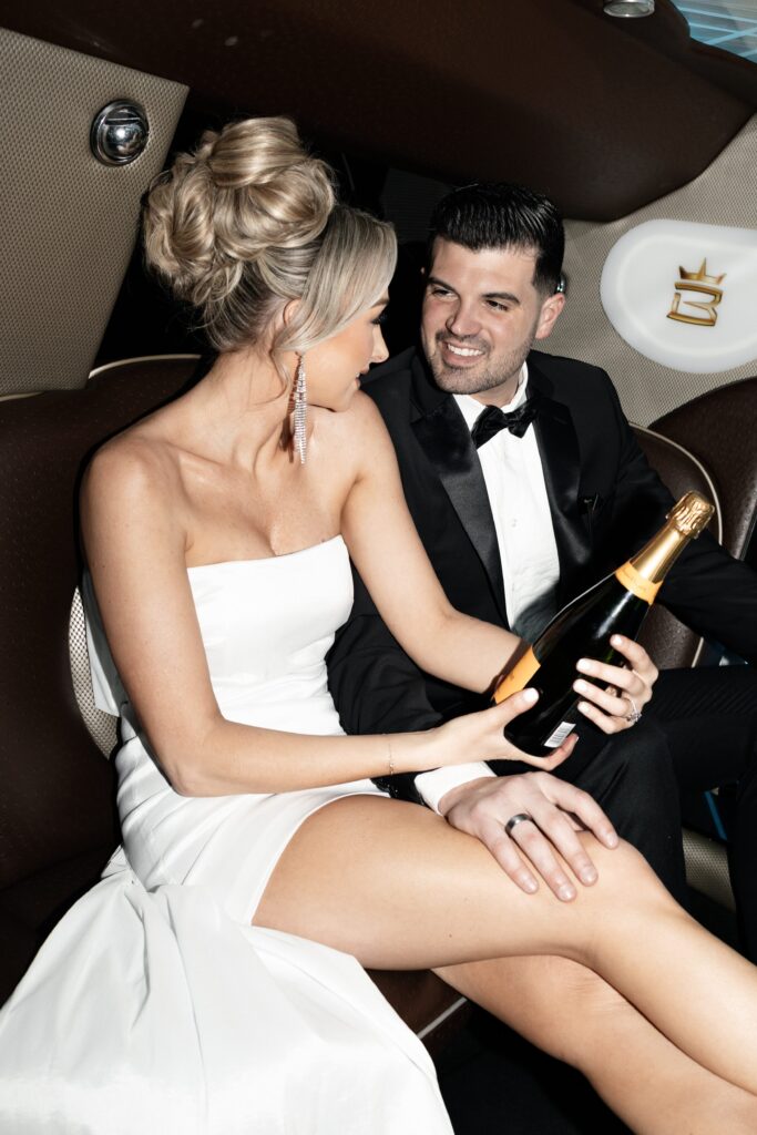 Bride and groom inside of their limo with a bottle of champagne 