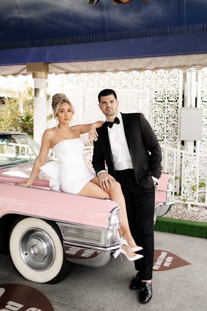 Bride sitting on the iconic pink Cadillac next to her groom at The Tunnel of Love for their elopement in Vegas