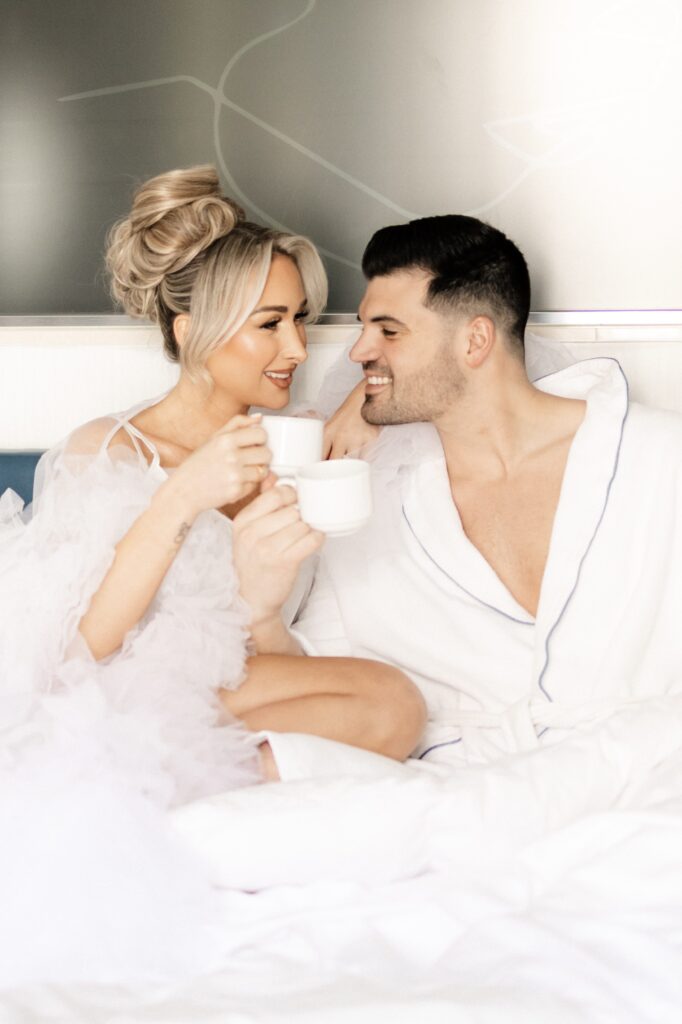 Bride and groom laying in bed wearing robes and drinking coffee