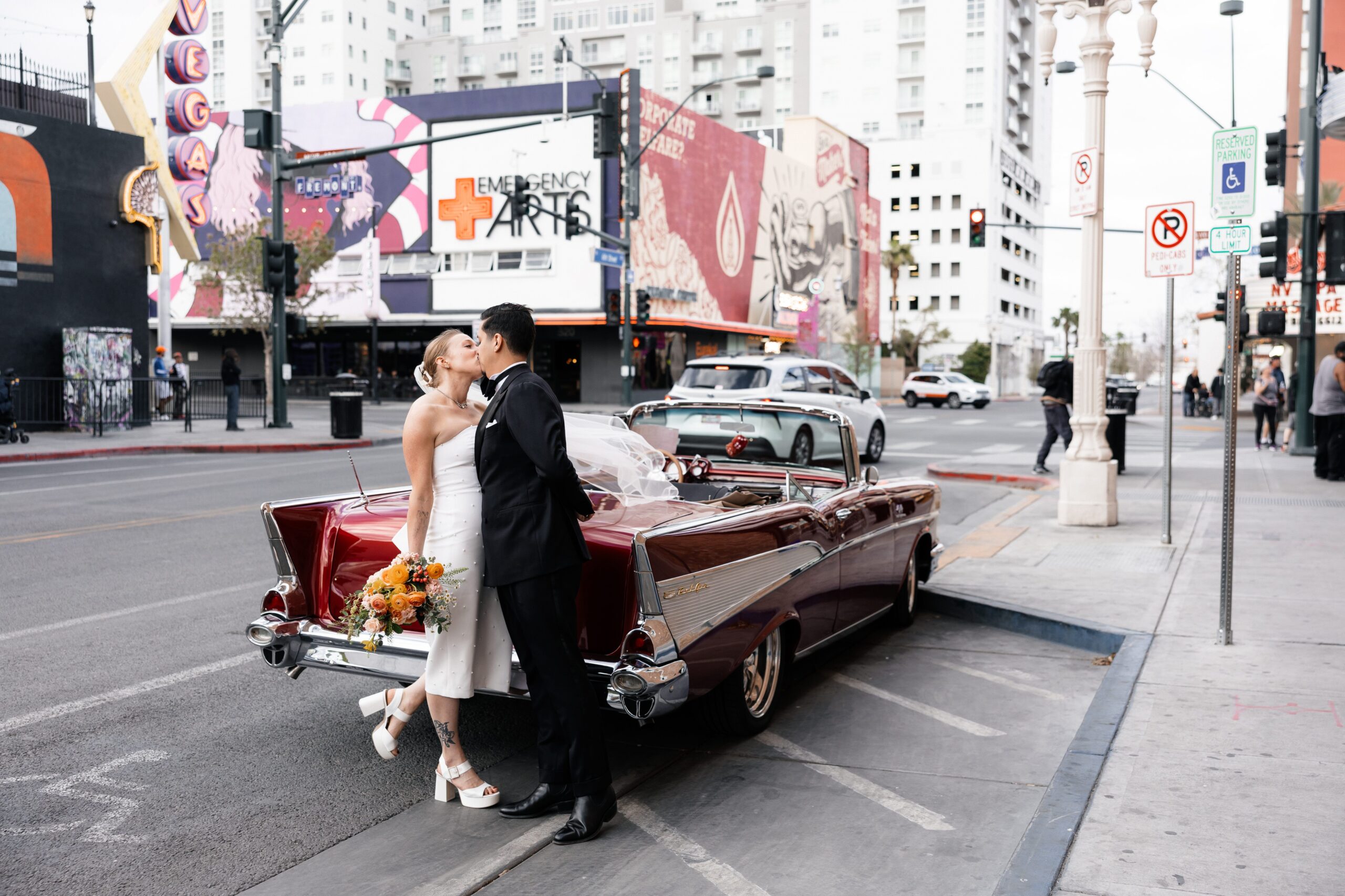 Bride and groom kissing next to a cherry red classic Chevrolet for their Las Vegas elopement wedding portraits 
