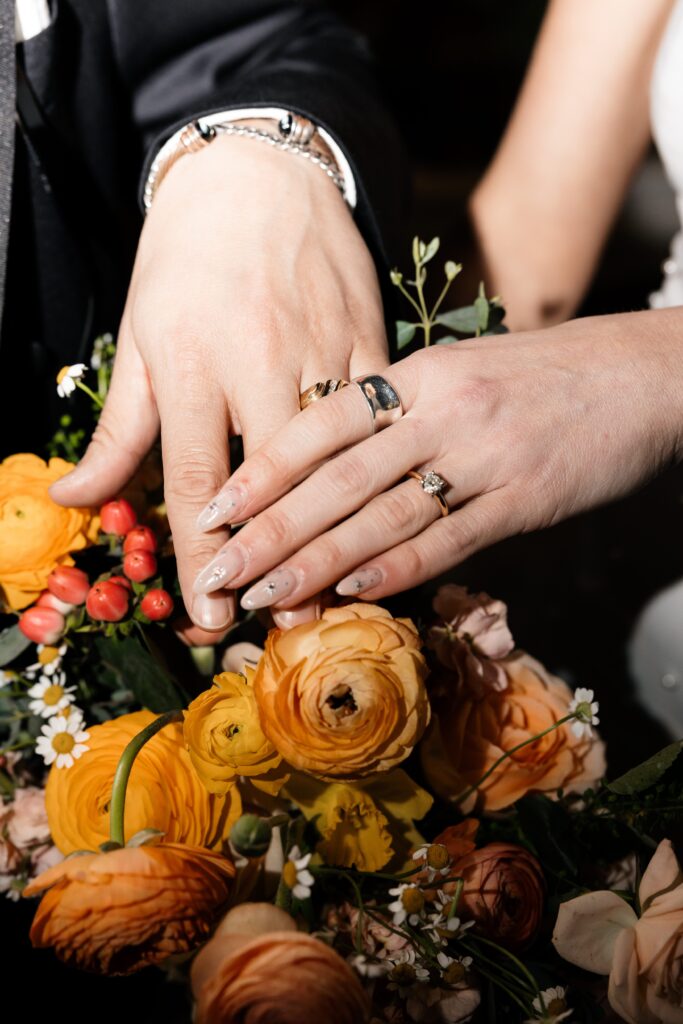 Flash photo of a bride and grooms hands over a wedding bouquet to show off their rings