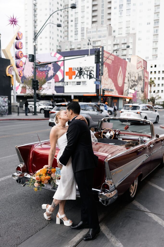 Bride and groom kissing next to a cherry red classic Chevrolet for their Las Vegas elopement wedding portraits 