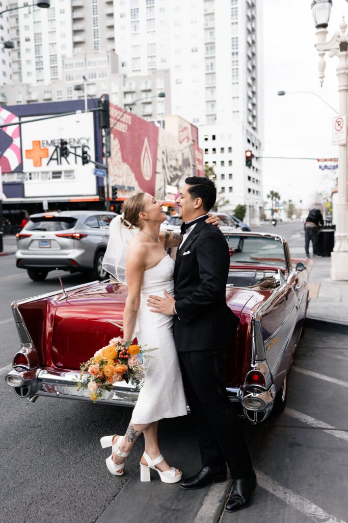 Bride and groom posing with a cherry red classic Chevrolet for their Las Vegas wedding portraits
