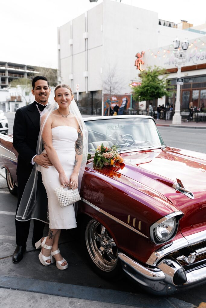 Bride and groom smiling next to a cherry red classic Chevrolet for their Las Vegas elopement wedding portraits 