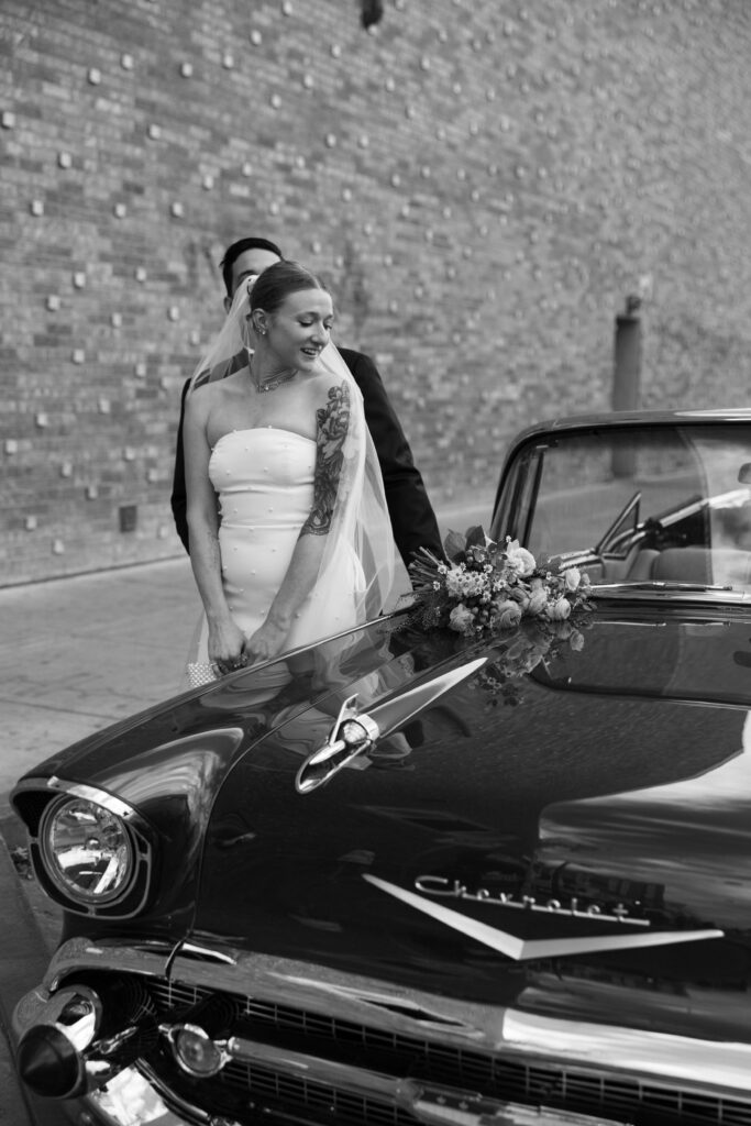 Black and white photo of a bride and groom posing next to a classic Chevrolet car for their Las Vegas elopement wedding portraits