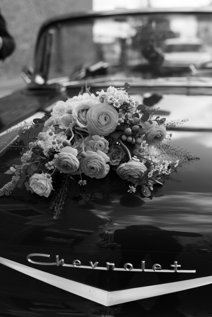 Black and white photo of a wedding bouquet on top of a classic Chevrolet