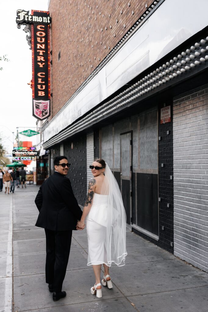 Bride and groom walking down Fremont Street  wearing sunglasses