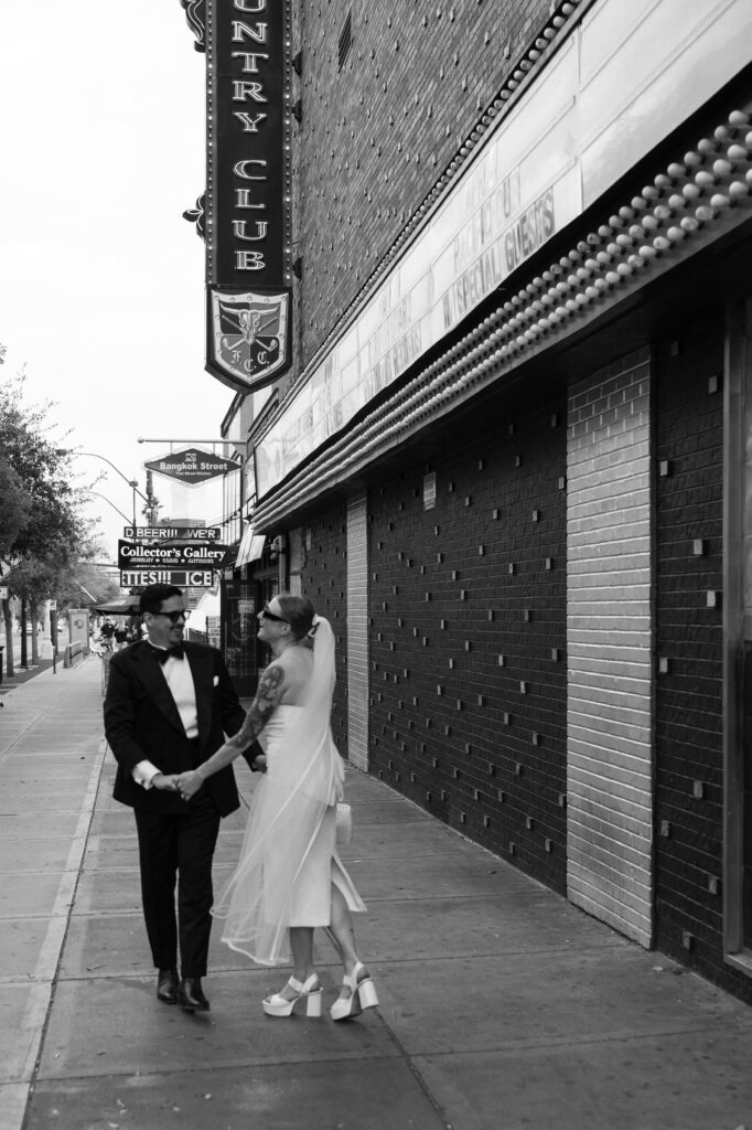 Black and white photo of a bride and groom being playful while walking down Fremont Street