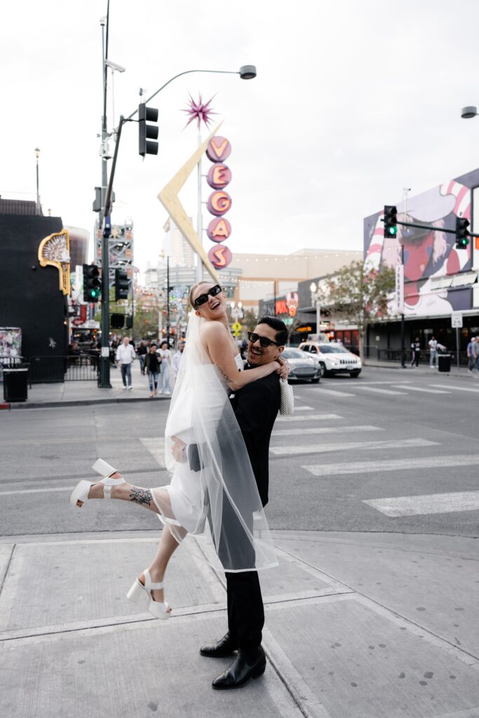 Groom holding up his bride in front of the iconic neon Vegas sign.