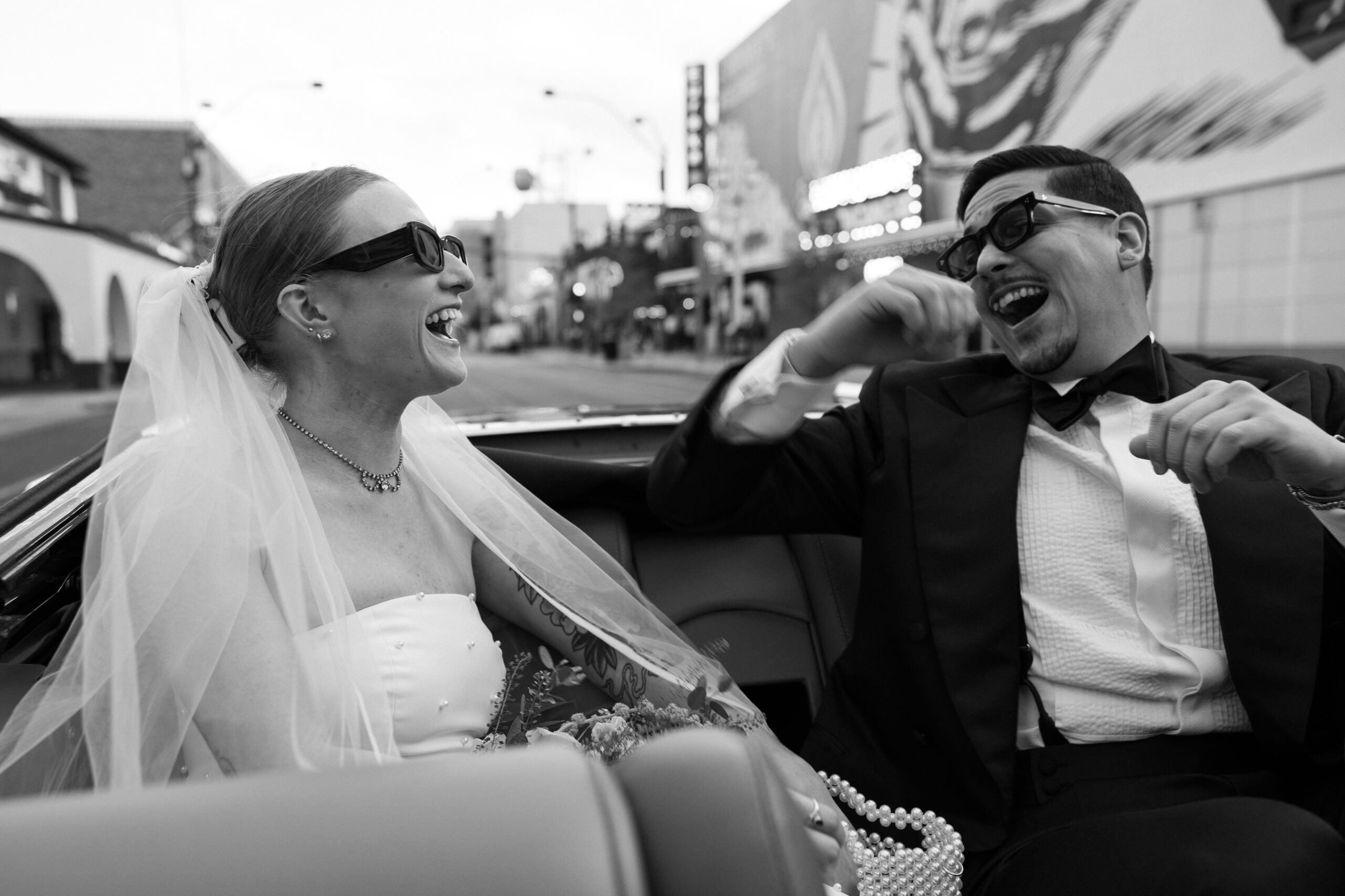 Black and white photo of a bride and groom laughing in a classic car during their Las Vegas elopement wedding