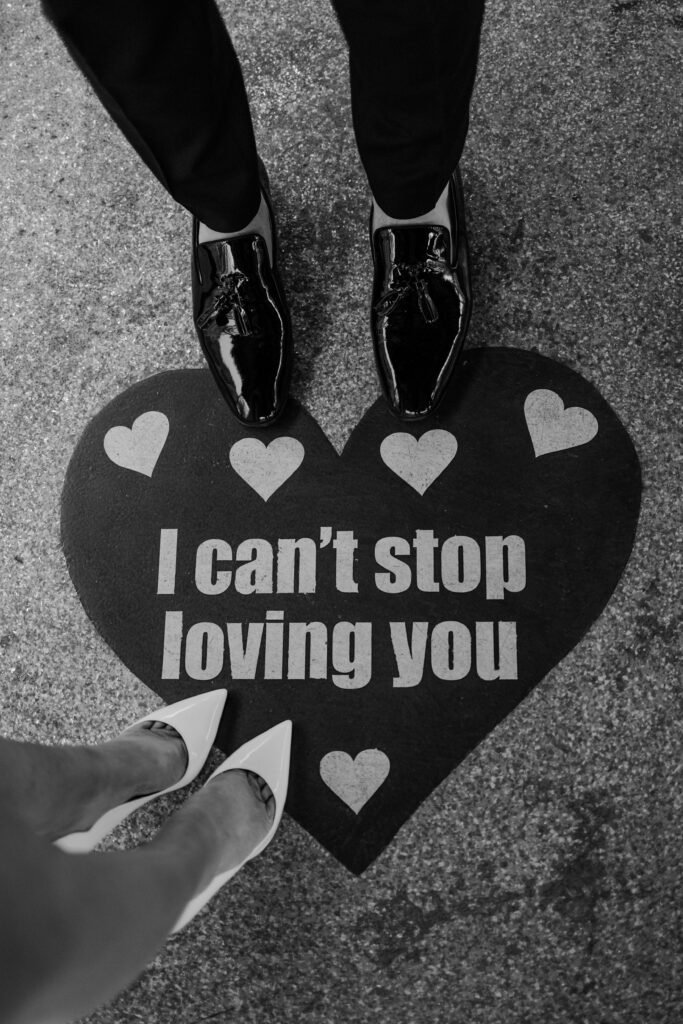 Black and white photo of a bride and groom standing on the " I can't Stop Loving You" heart at The Little White Chapel
