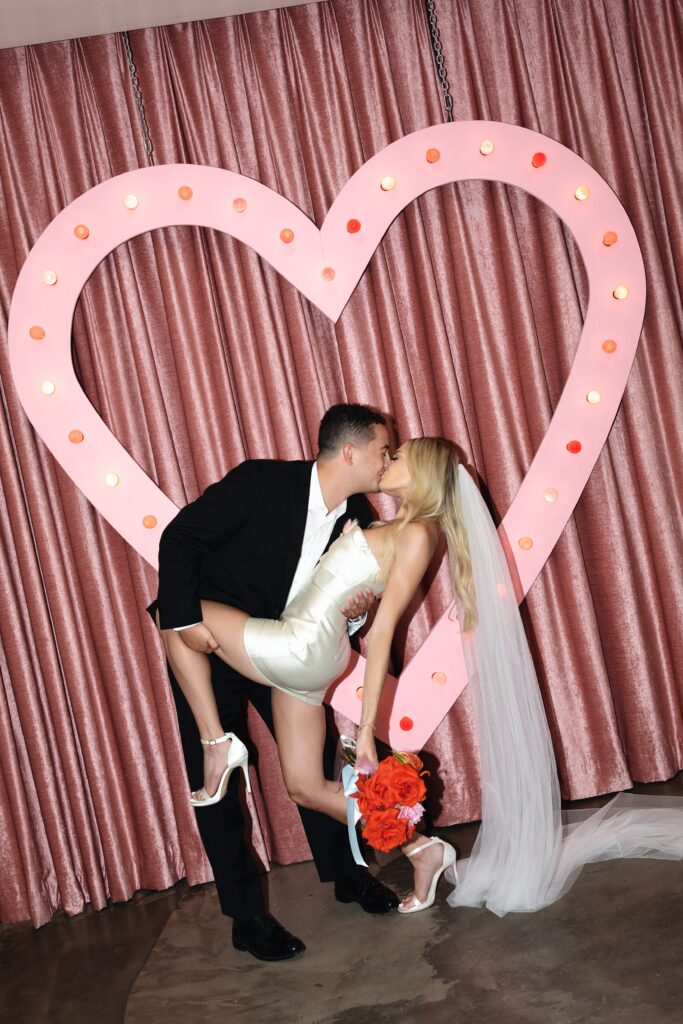 Bride and groom kissing in front of the neon pink heart at Sure Thing Chapel