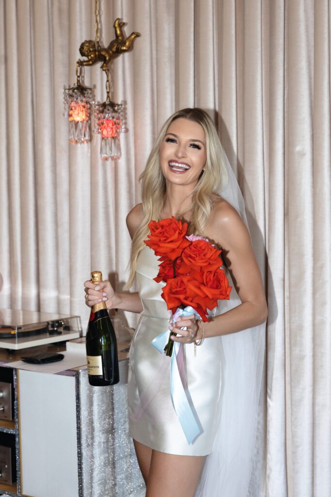 Bride holding her red bouquet and a bottle of champagne