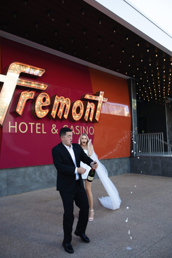 Bride and groom popping champagne in front of Fremont Hotel and Casino