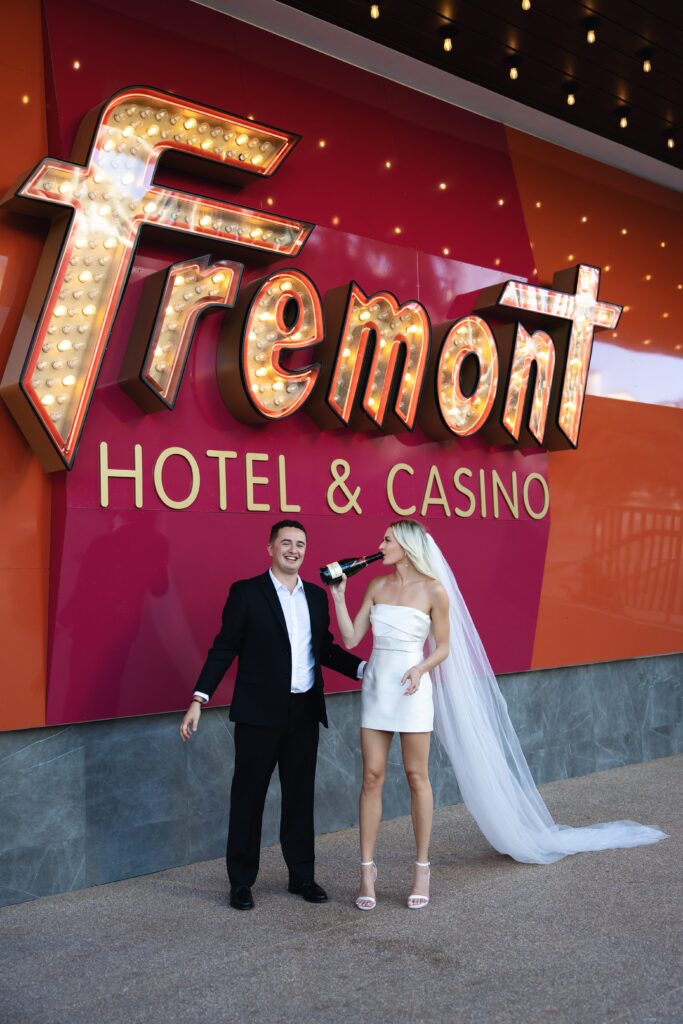 Bride drinking champagne straight from the bottle in front of Fremont Hotel and Casino