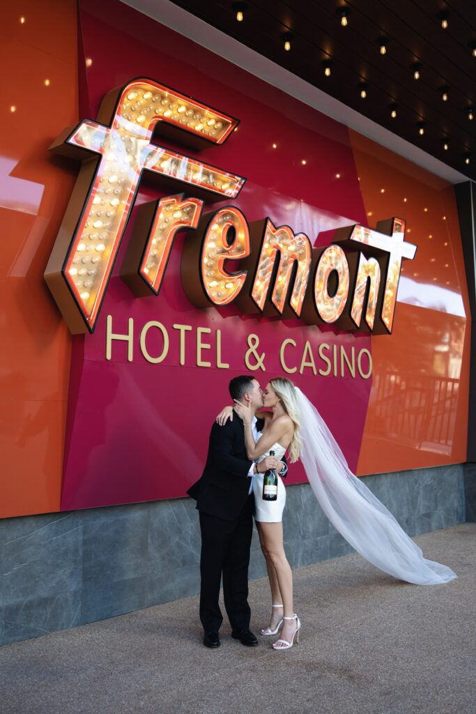 Bride and groom kissing with a bottle of champagne in front of Fremont Hotel and Casino