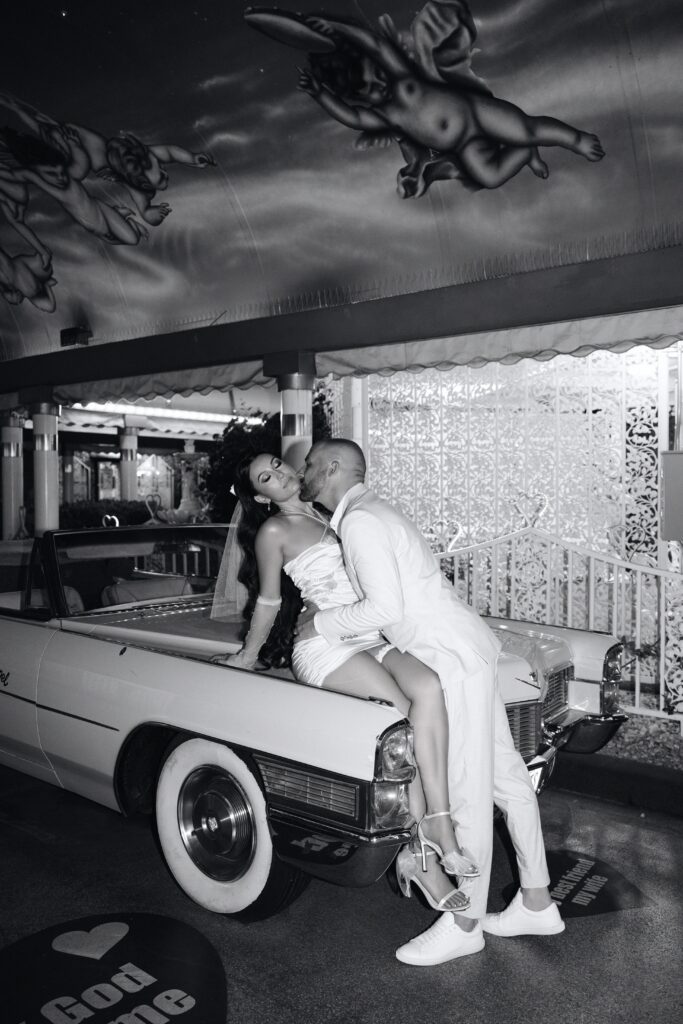 Black and white photo of a bride and groom with the Pink Cadillac at Little White Wedding Chapel
