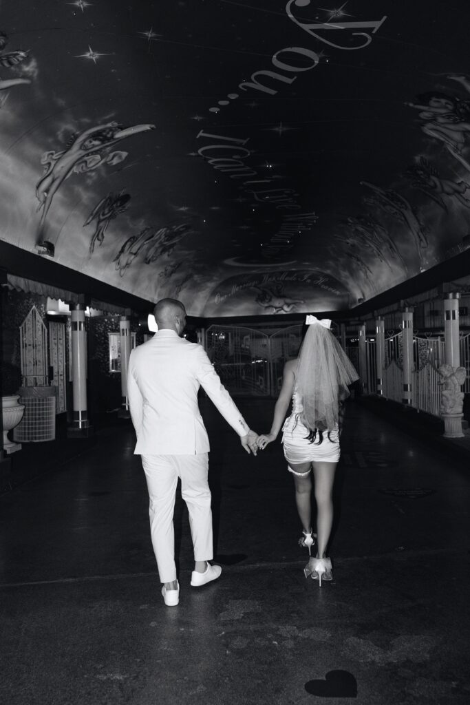 Black and white photo of a bride and groom holding hands in The Tunnel of Love at Little White Wedding Chapel