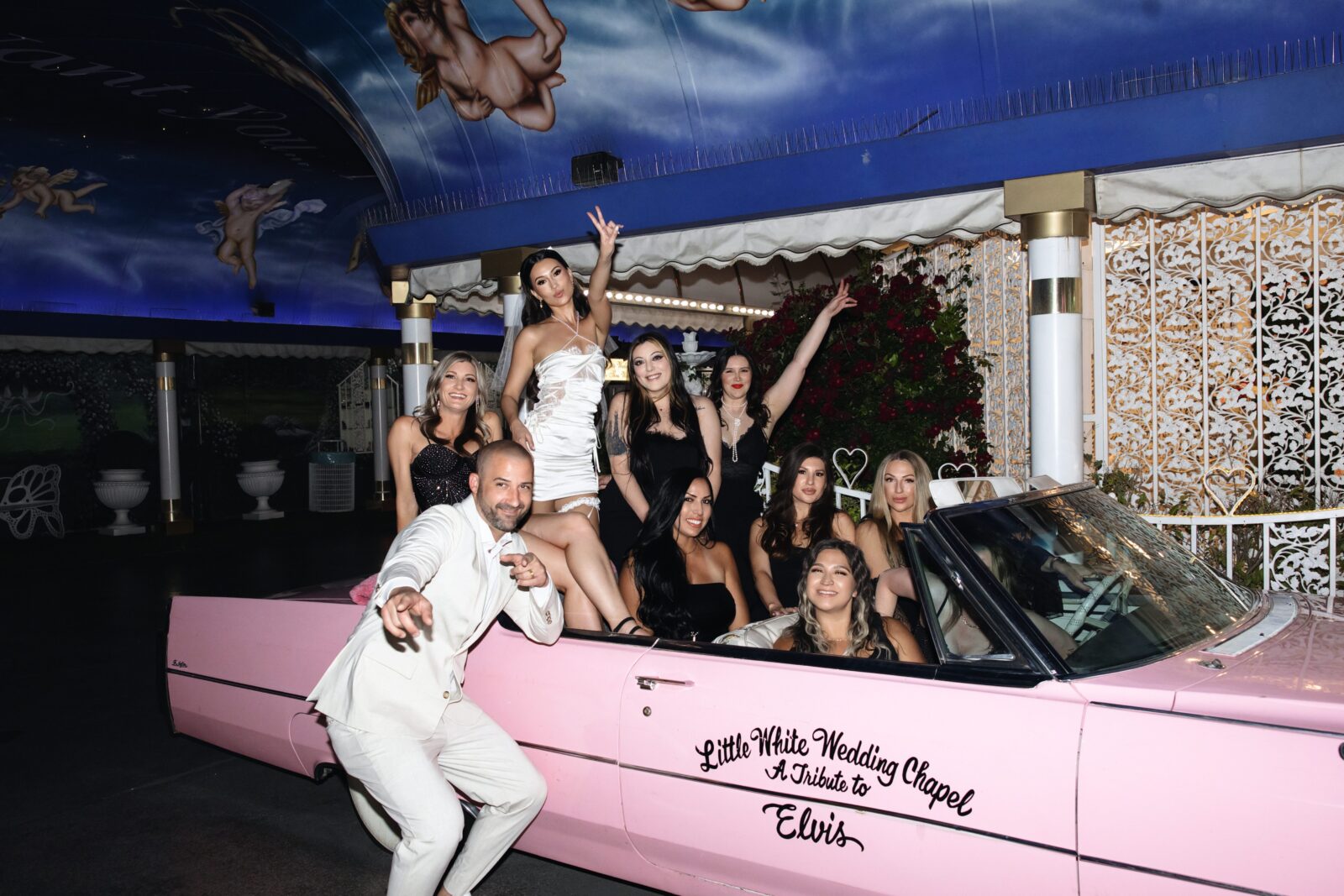 Bride, groom and their wedding party posing for photos in the Pink Cadillac at Little White Wedding Chapel in Las Vegas