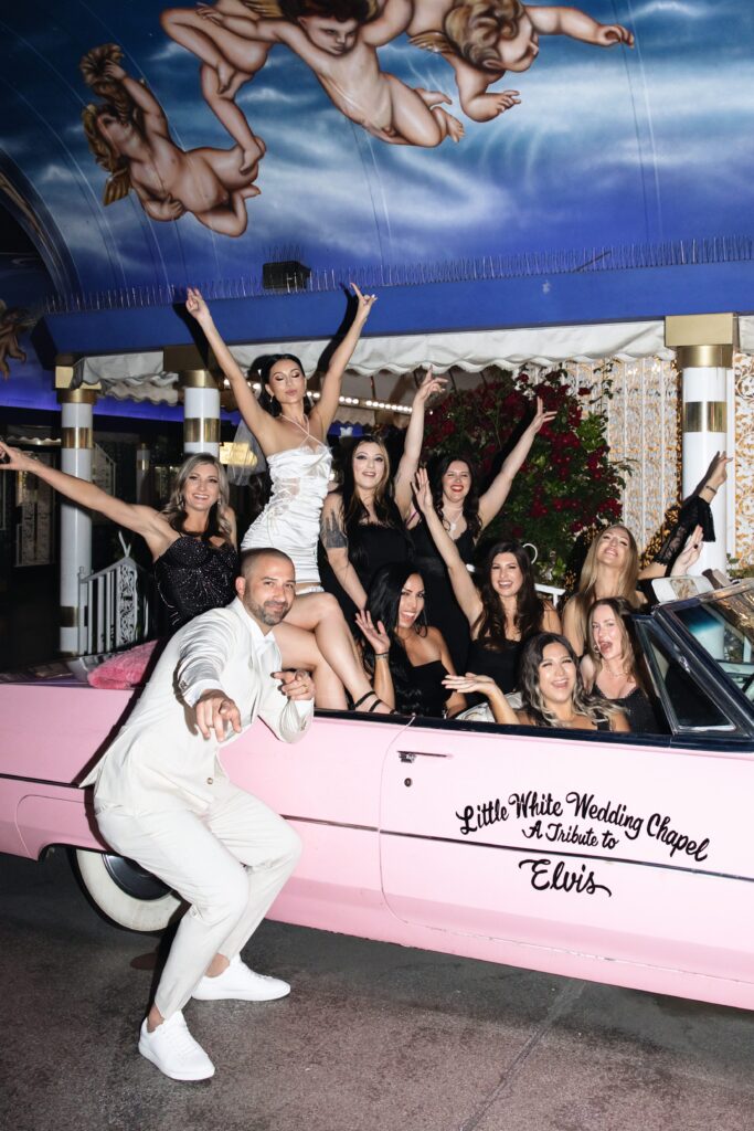 Bride, groom and their wedding party posing inside of Little White Wedding Chapels Pink Cadillac