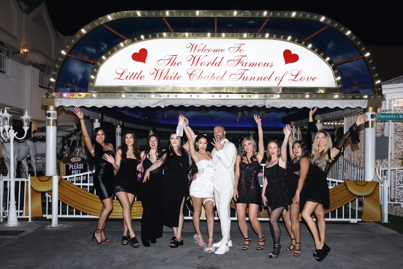 Bride, groom and their bachelorette party posing for portraits in front of Little White Wedding Chapels Tunnel of Love