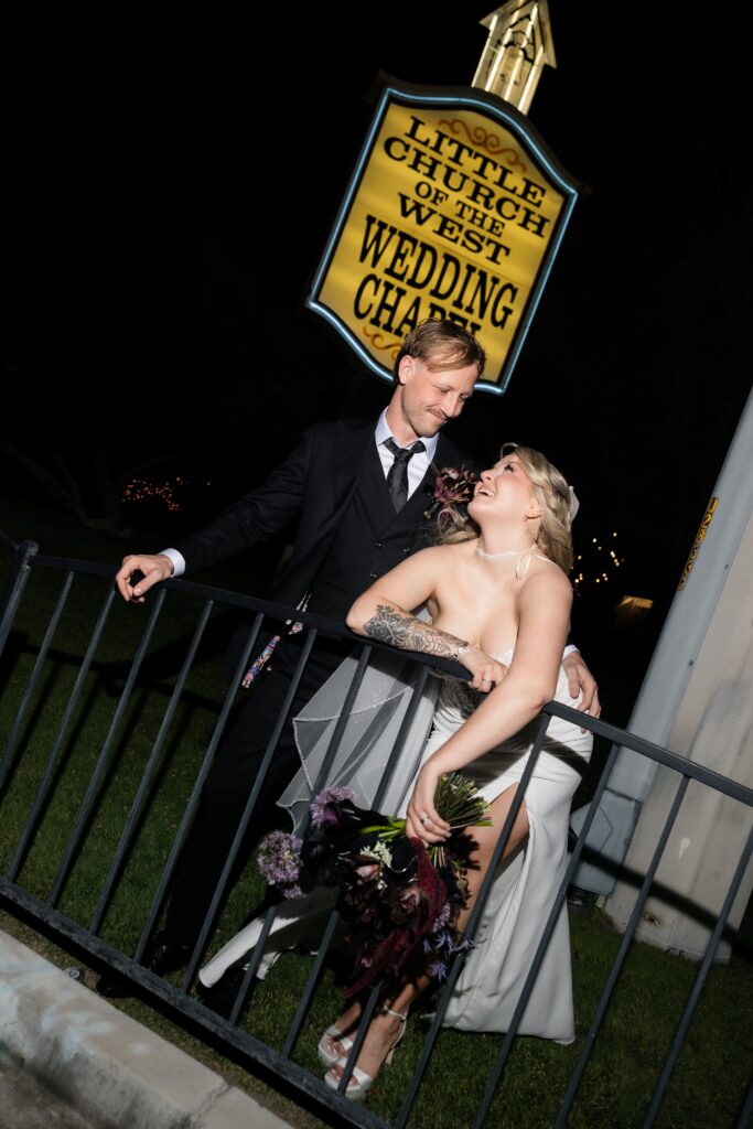 Bride and groom posing outside in front of the The Little Church of The West sign at night.