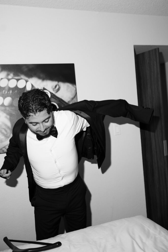 Black and white photo of a groom getting ready and putting his jacket on