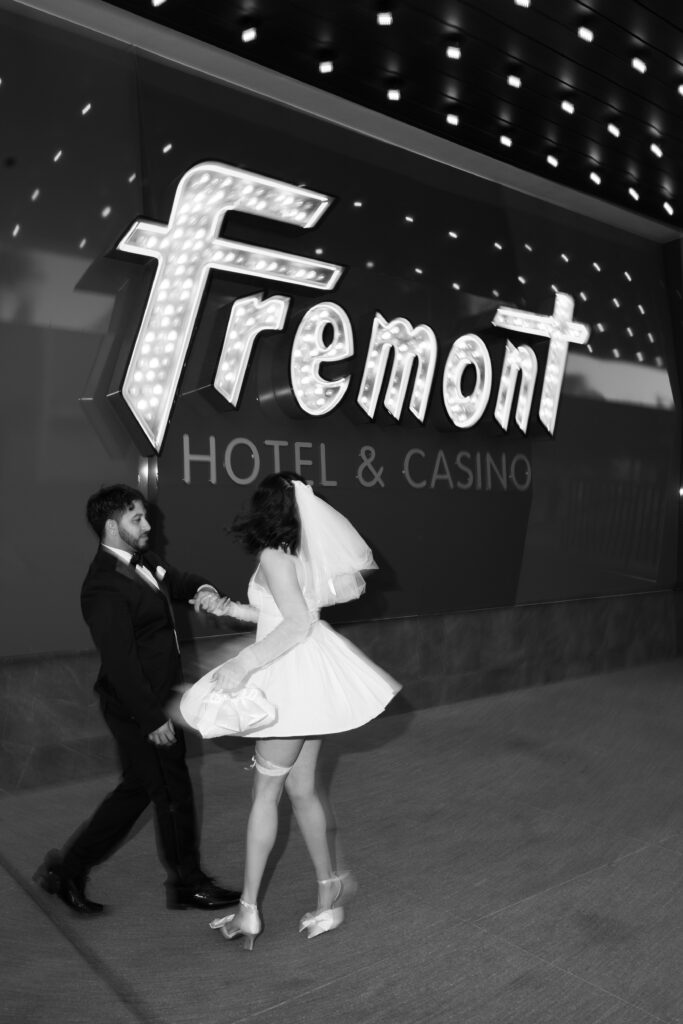 Black and white photo of a bride and groom dancing in front of Fremont Hotel & Casino sign