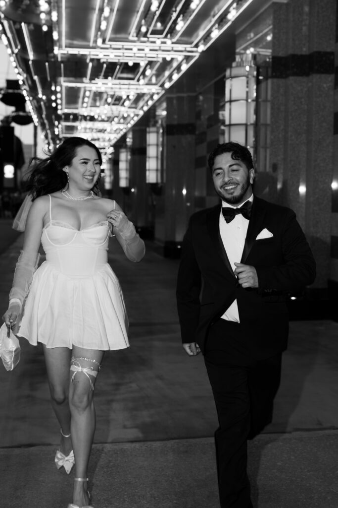 Black and white elopement photo of a bride and groom running down Fremont Street for their fun Vegas elopement