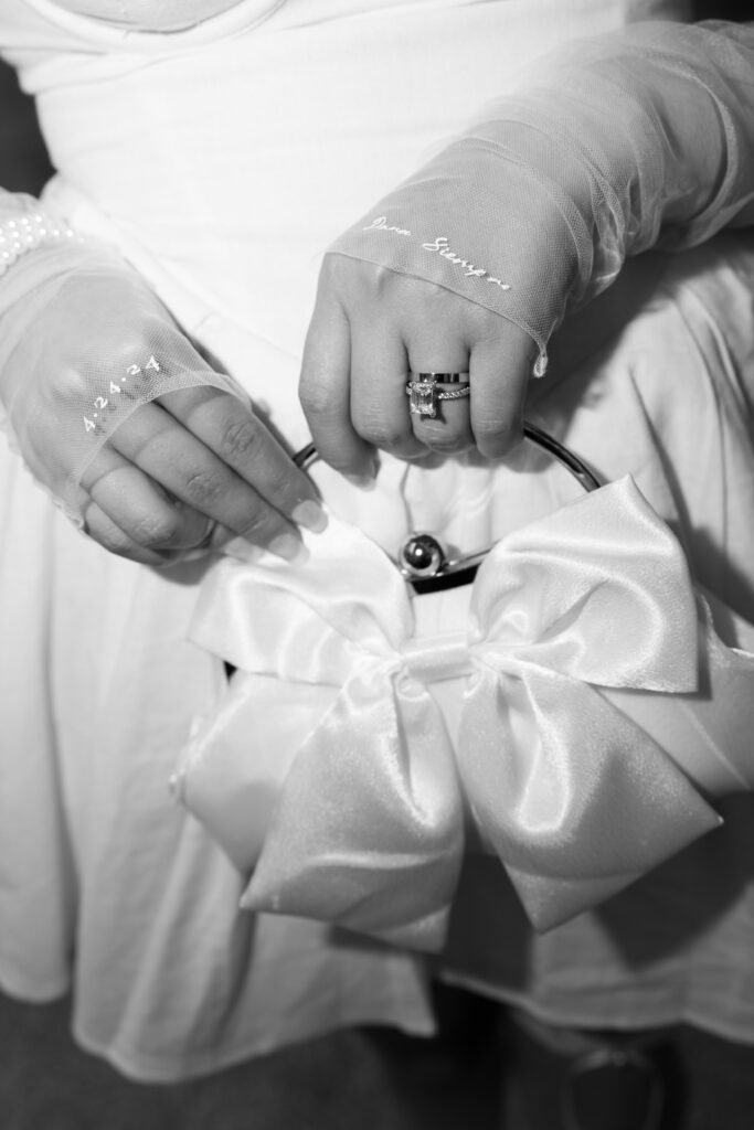 Black and white photo of a bride wearing a short white dress with sheer sleeves and a little white purse with a bow