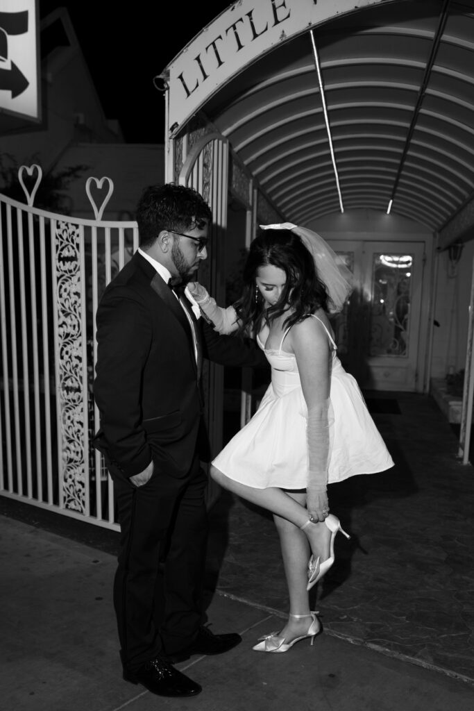 Black and white editorial elopement photo of a bride fixing her heels at Little White Wedding Chapel in Las Vegas