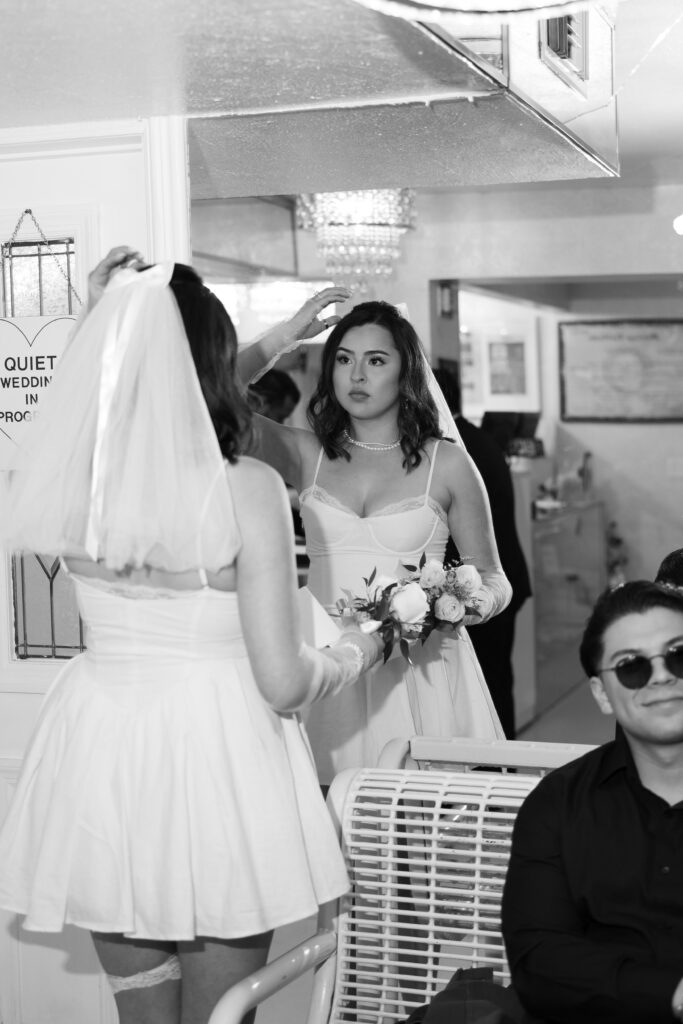 Black and white photo of a bride fixing her veil in the mirror before her Little White Wedding Chapel ceremony