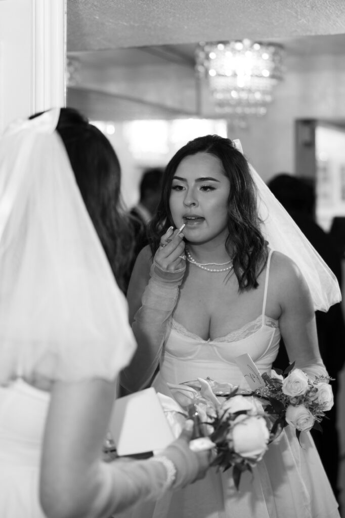 Black and white photo of a bride reapplying her lipstick in the mirror before her Little White Wedding Chapel ceremony