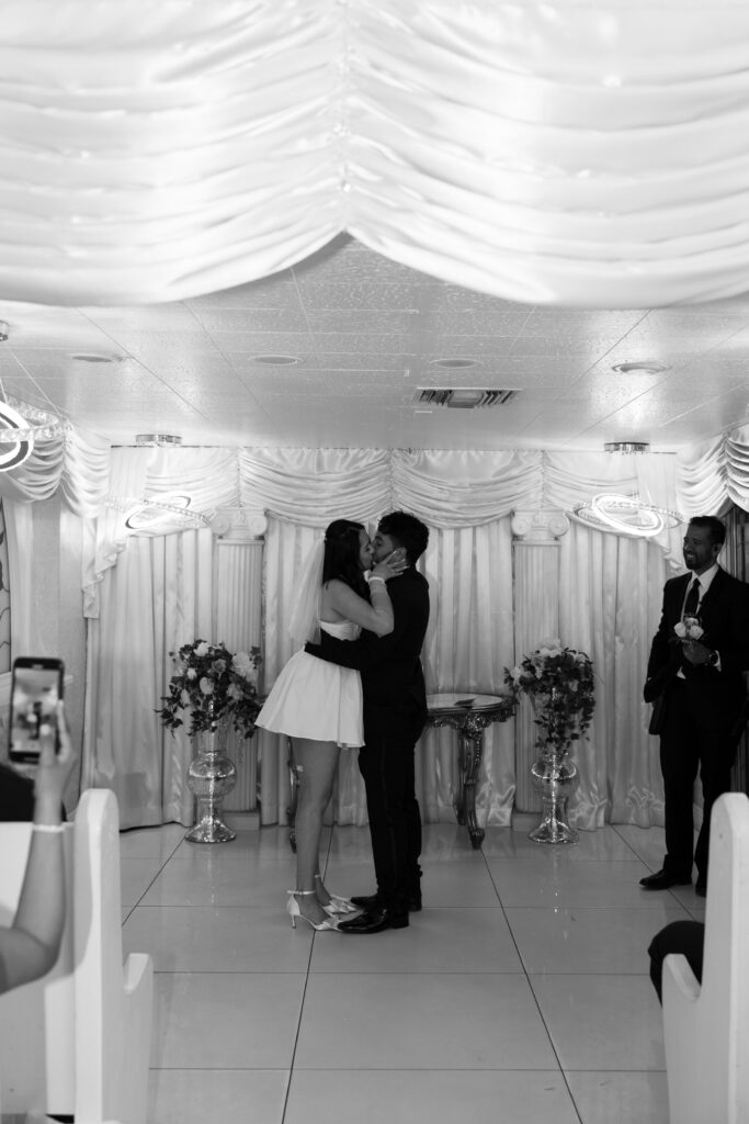 Black and white photo of a bride and groom kissing at the end of their Little White Wedding Chapel ceremony