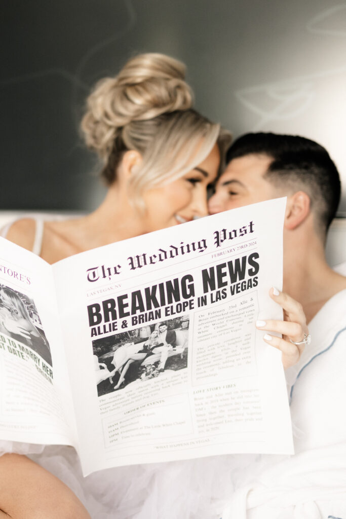 Bride and groom smiling at each other as the bride holds up a wedding newspaper that says "Breaking News" for their elopement announcement 