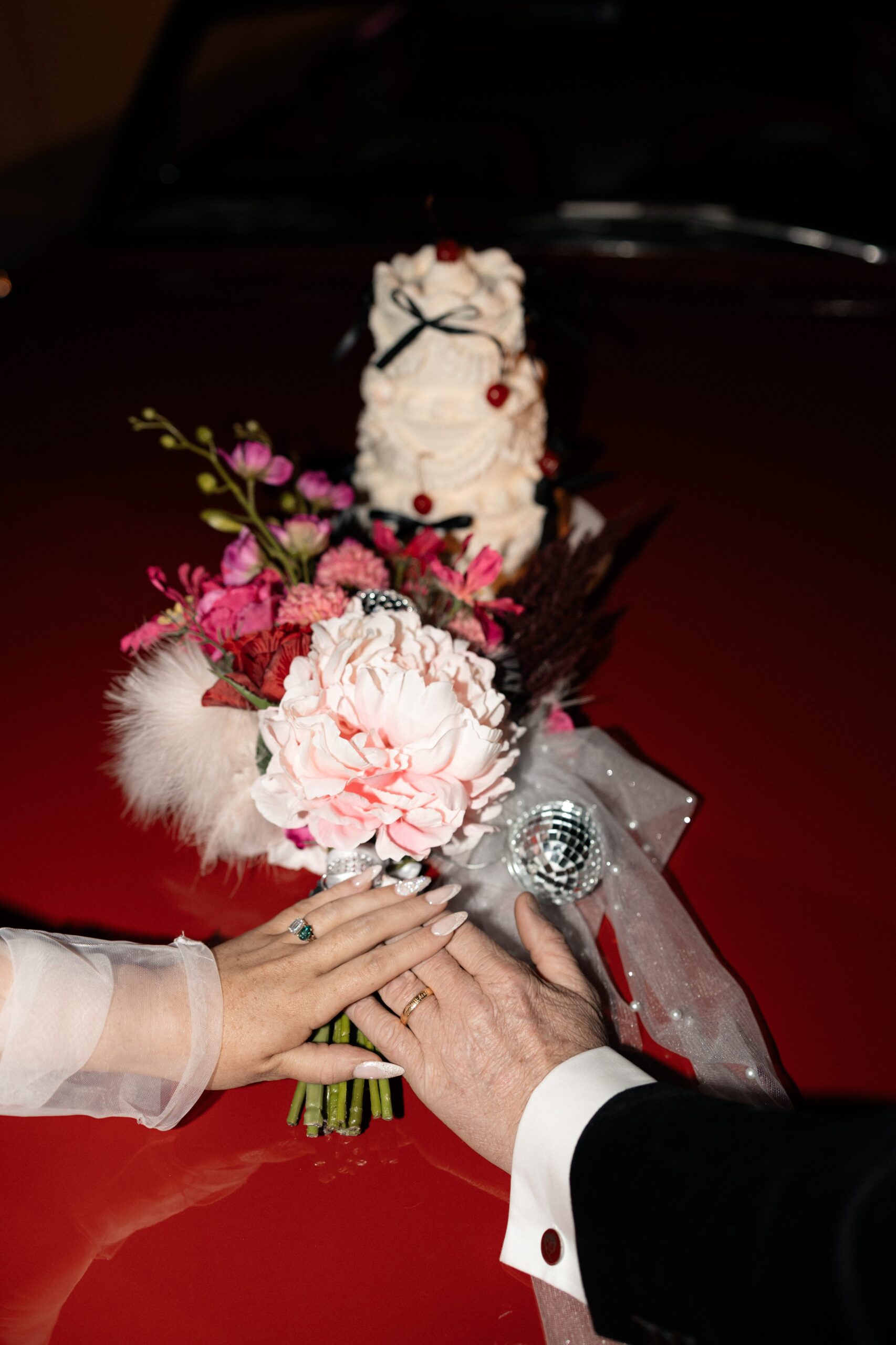 Photo of a bride and groom holdings hands with a cake and wedding bouquet in the background