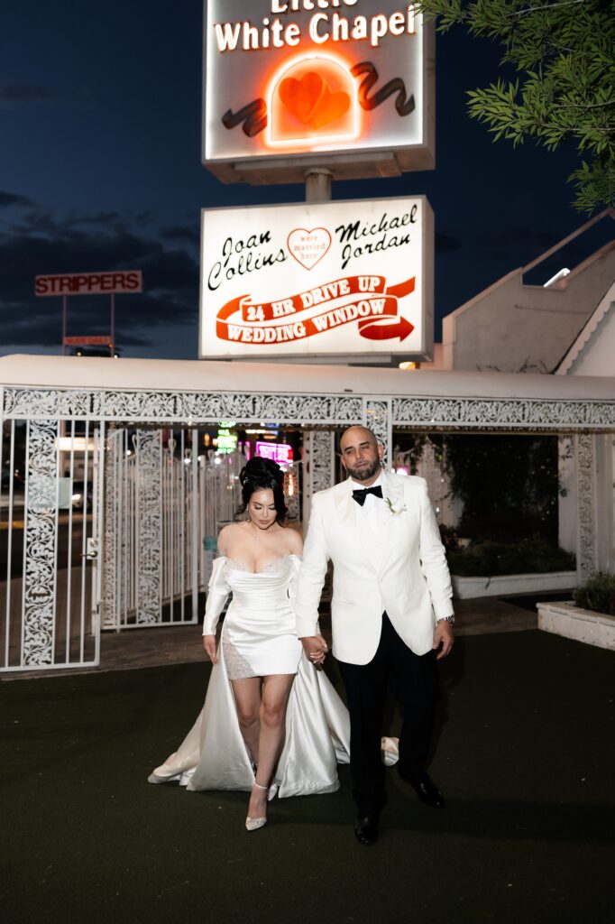 Bride and groom posing in front of The Little White Wedding Chapel sign