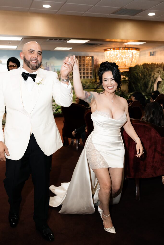 Bride and groom holding hands as they walk back down the aisle after their Elvis wedding ceremony in Chapel Amore at The Little White Wedding Chapel