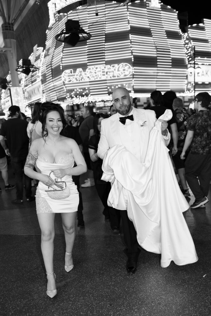 Black and white photo of a bride and groom walking on Fremont Street during their downtown Vegas elopement