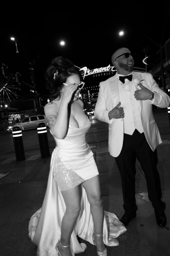 Black and white paparazzi style elopement photo of a bride and groom on Fremont Street for their downtown Vegas elopement