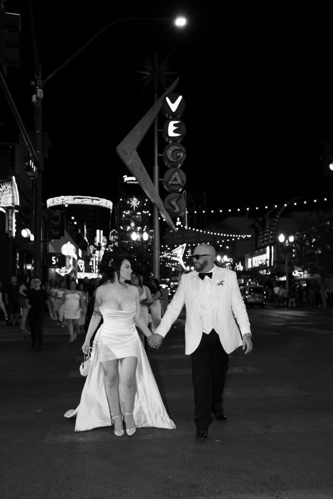 Black and white photo of a bride and groom holding hands and walking on Fremont Street for their downtown Vegas elopement