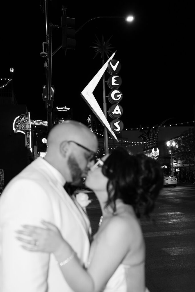 Black and white photo of a bride and groom kissing in front of the Vegas sign on Fremont Street for their downtown Vegas elopement