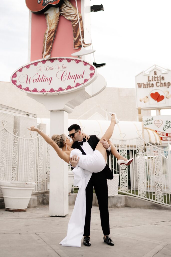 Bride and groom posing in front of the Little White Wedding Chapel sign