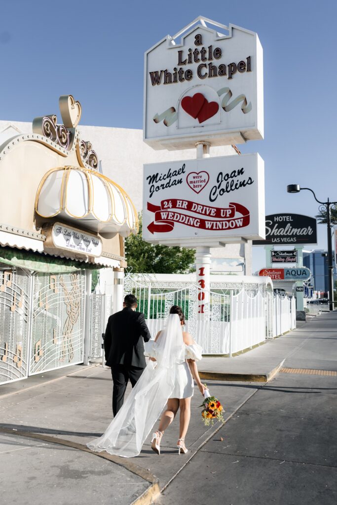 Bride and grooms walking in front of a Little White Chapel sign in Las Vegas