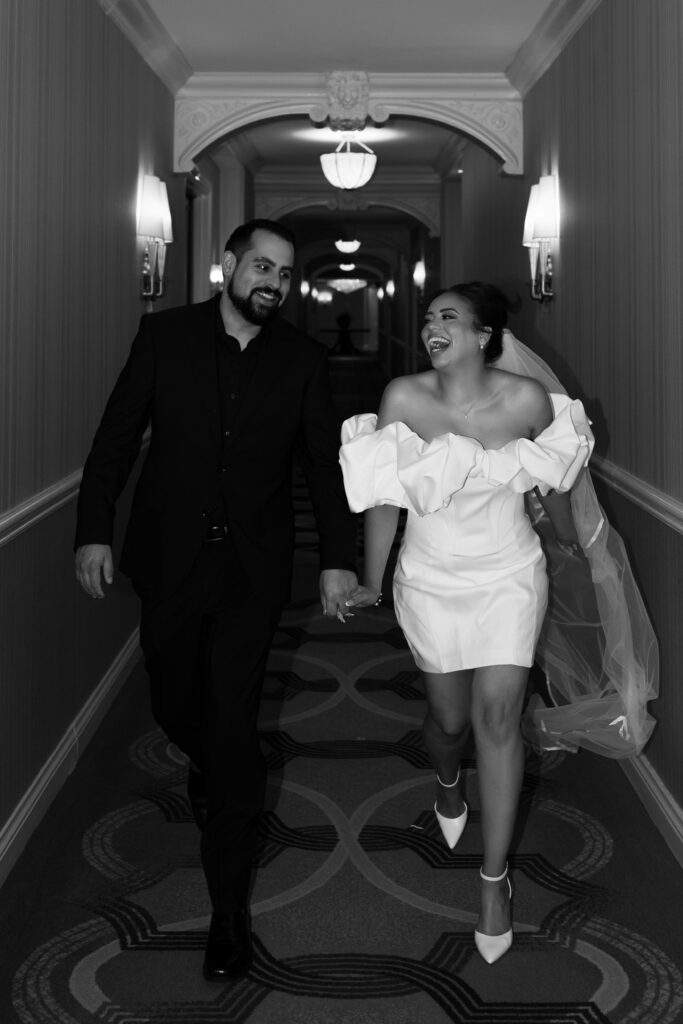 Black and white photo of a bride and groom laughing as they run down the hallways at The Venetian in Las Vegas