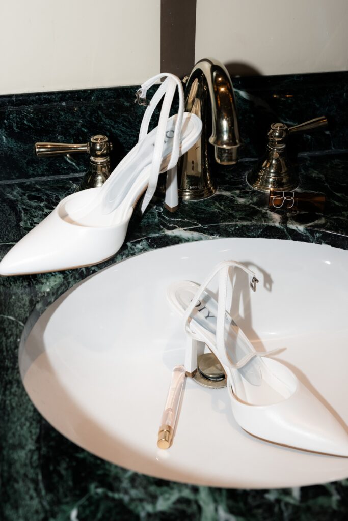 Detail shot of a brides heels and perfume in the sink