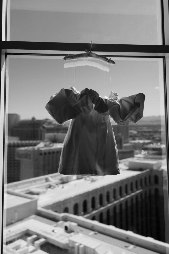 Black and white photo of a brides short elopement dress hanging on the window of their suite at The Venetian