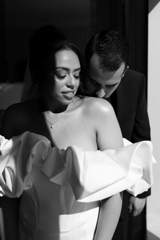 Black and white photo of a groom kissing his brides shoulder